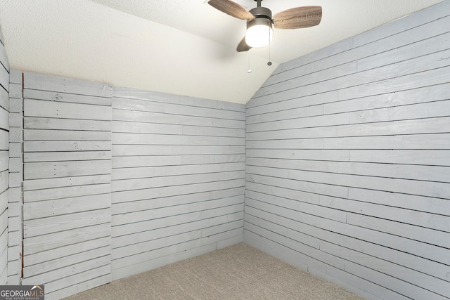 interior space with lofted ceiling, wooden walls, ceiling fan, and a textured ceiling