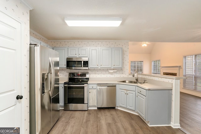 kitchen with light hardwood / wood-style floors, vaulted ceiling, kitchen peninsula, sink, and appliances with stainless steel finishes