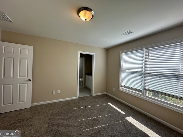 unfurnished bedroom with multiple windows, connected bathroom, and dark colored carpet