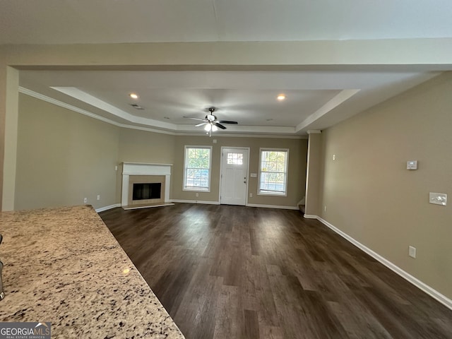 unfurnished living room with ornamental molding, a raised ceiling, ceiling fan, and dark hardwood / wood-style flooring