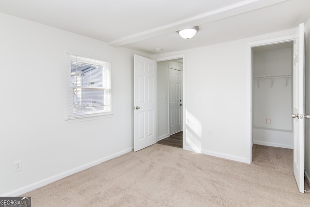 unfurnished bedroom with light colored carpet, a walk in closet, and a closet