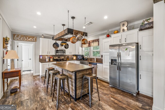 kitchen with stainless steel appliances, dark wood-type flooring, white cabinets, and decorative light fixtures