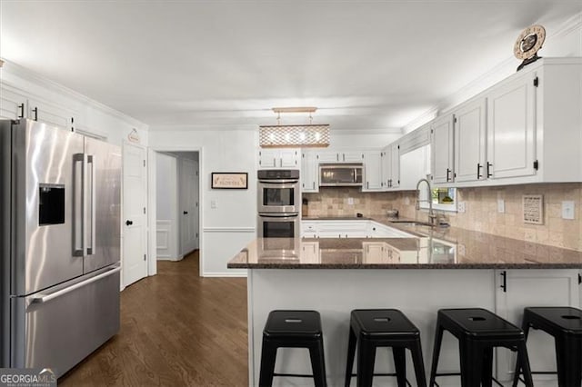 kitchen featuring stainless steel appliances, dark hardwood / wood-style flooring, a breakfast bar, white cabinetry, and dark stone countertops