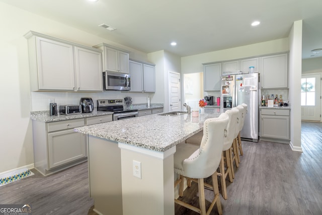 kitchen with appliances with stainless steel finishes, sink, light hardwood / wood-style floors, a breakfast bar area, and a center island with sink