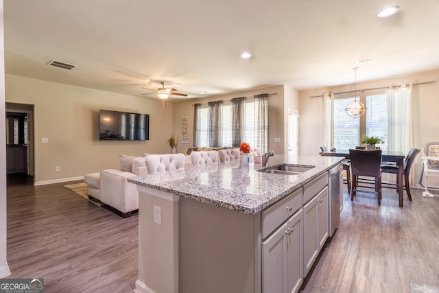 kitchen with sink, decorative light fixtures, light stone counters, hardwood / wood-style flooring, and a kitchen island with sink