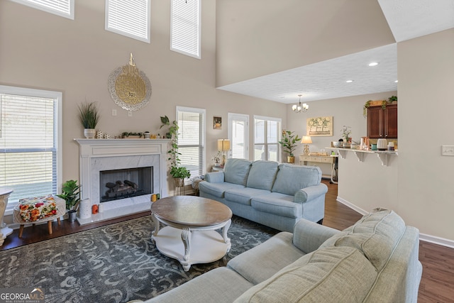 living room featuring a towering ceiling, a notable chandelier, dark hardwood / wood-style floors, and a high end fireplace