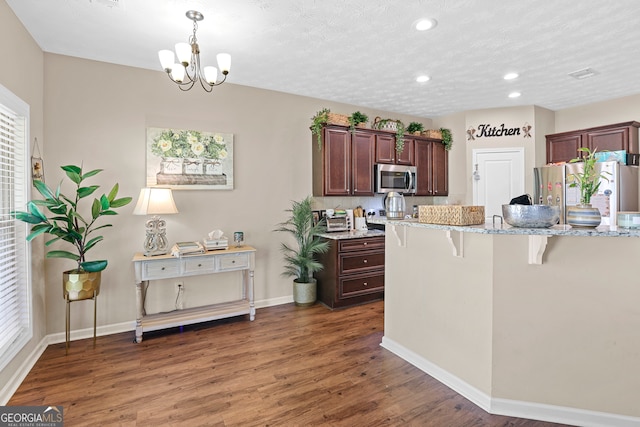 kitchen featuring appliances with stainless steel finishes, light stone countertops, a kitchen breakfast bar, and dark hardwood / wood-style flooring