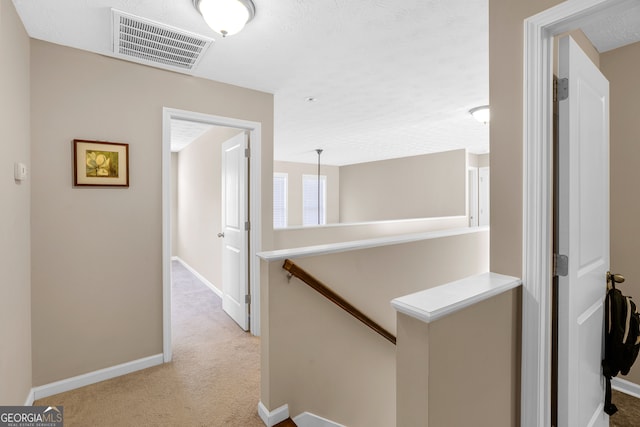 hall with a textured ceiling and light colored carpet