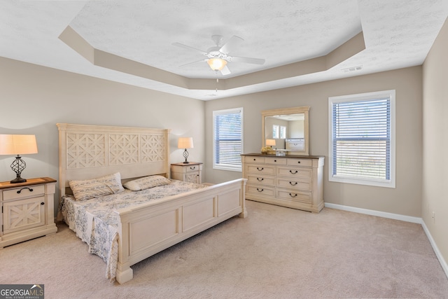 carpeted bedroom with a textured ceiling, a raised ceiling, multiple windows, and ceiling fan