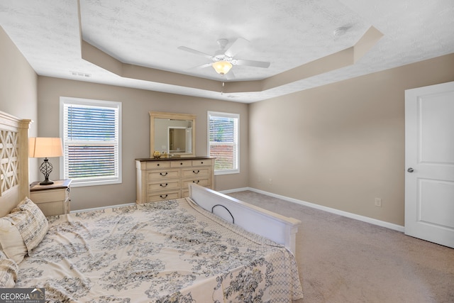 carpeted bedroom featuring multiple windows, a textured ceiling, a tray ceiling, and ceiling fan