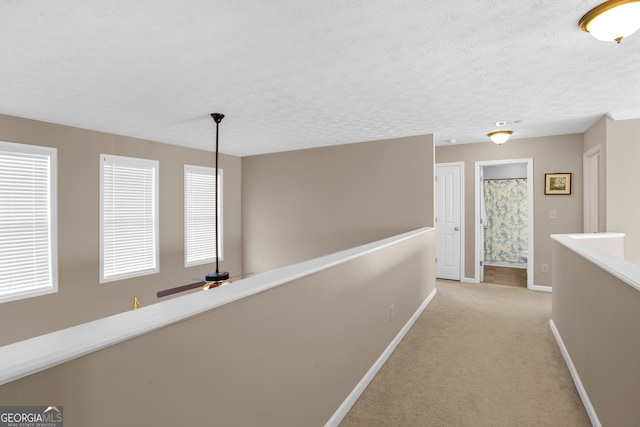 hallway with a textured ceiling and light colored carpet