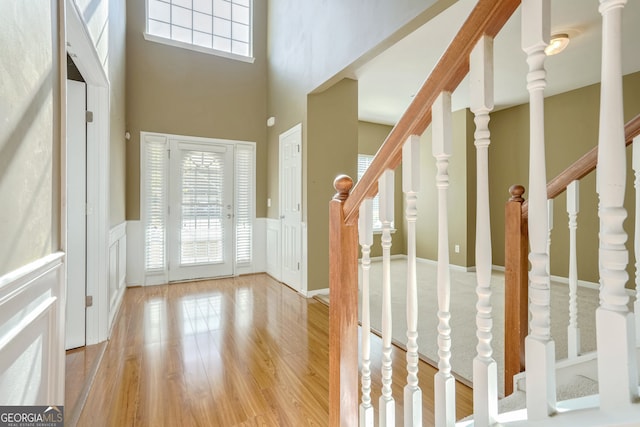 foyer entrance featuring a towering ceiling, light hardwood / wood-style flooring, and a wealth of natural light