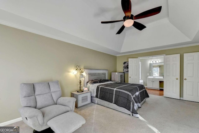 carpeted bedroom featuring crown molding, ensuite bathroom, a tray ceiling, and ceiling fan