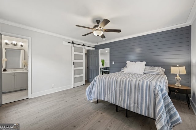 bedroom with ensuite bath, ceiling fan, crown molding, a barn door, and light hardwood / wood-style floors