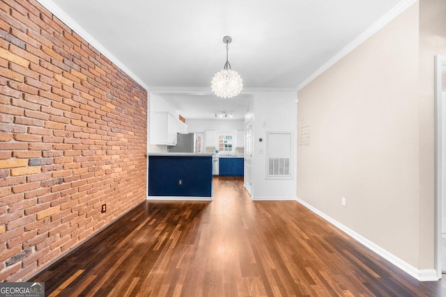 unfurnished living room with brick wall, dark wood-type flooring, ornamental molding, and a chandelier