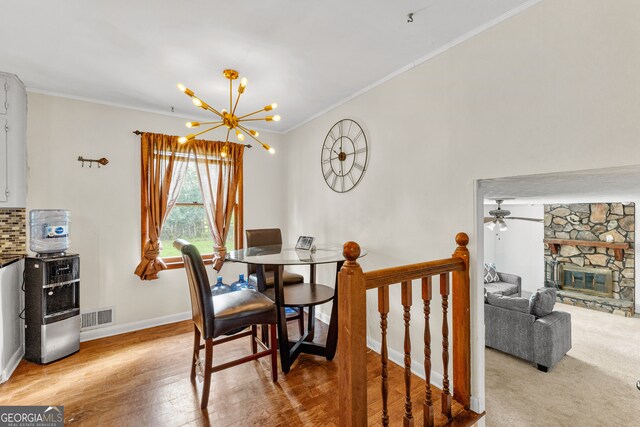 dining space featuring a stone fireplace, ornamental molding, ceiling fan with notable chandelier, and light wood-type flooring