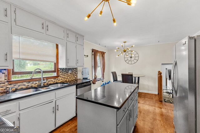 kitchen with appliances with stainless steel finishes, sink, light wood-type flooring, a center island, and decorative backsplash