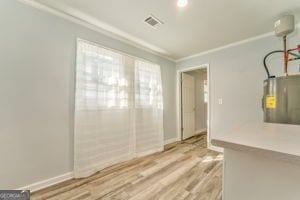 interior space with electric water heater, ornamental molding, and light hardwood / wood-style floors