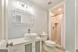 bathroom with crown molding, tiled shower, vanity, and toilet