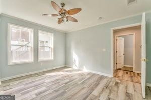 empty room with ornamental molding, ceiling fan, and light wood-type flooring