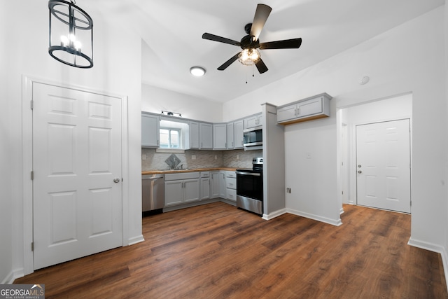 kitchen featuring ceiling fan with notable chandelier, stainless steel appliances, decorative backsplash, gray cabinets, and dark hardwood / wood-style floors