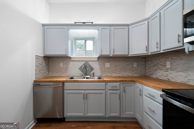 kitchen with stainless steel appliances, butcher block countertops, sink, and tasteful backsplash