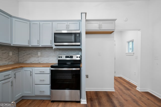 kitchen with gray cabinetry, dark hardwood / wood-style floors, backsplash, wood counters, and appliances with stainless steel finishes