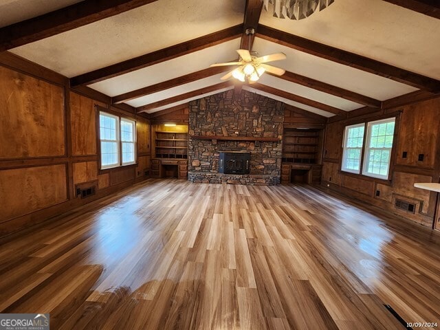 unfurnished living room with hardwood / wood-style flooring, wooden walls, lofted ceiling with beams, built in shelves, and ceiling fan