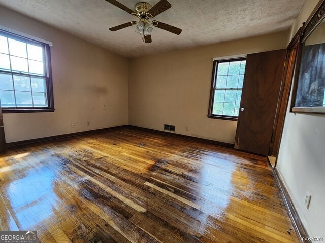 empty room featuring a barn door, ceiling fan, wood-type flooring, and plenty of natural light