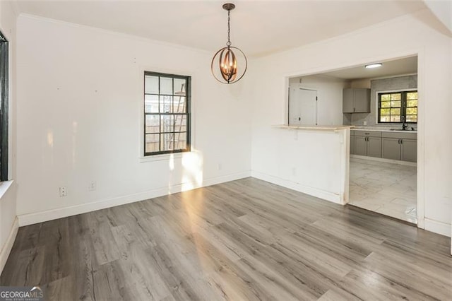 unfurnished dining area with ornamental molding, an inviting chandelier, hardwood / wood-style floors, and sink