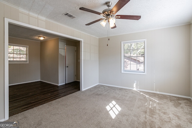 empty room featuring a healthy amount of sunlight, a textured ceiling, and dark colored carpet