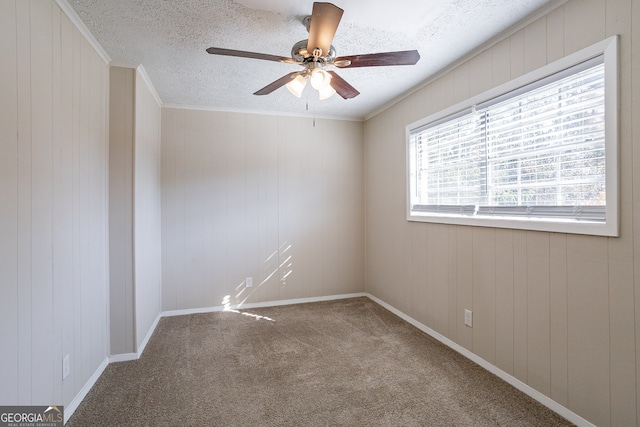 spare room with a textured ceiling, carpet floors, wooden walls, and ceiling fan