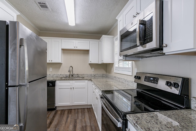 kitchen featuring dark wood-type flooring, ornamental molding, light stone countertops, white cabinetry, and appliances with stainless steel finishes