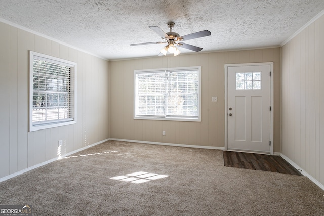 carpeted entrance foyer featuring wood walls, ornamental molding, ceiling fan, and a wealth of natural light