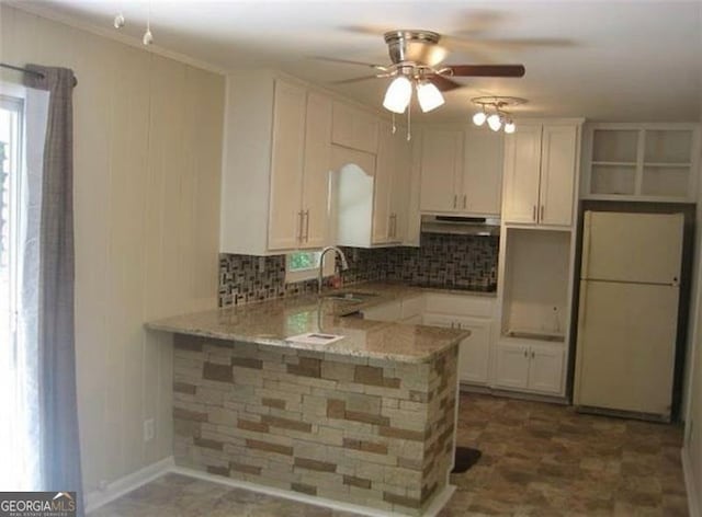 kitchen with kitchen peninsula, white cabinets, light stone countertops, sink, and white refrigerator