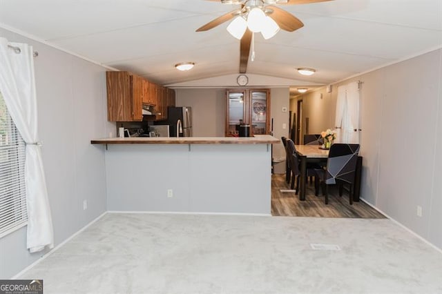 kitchen featuring light carpet, kitchen peninsula, stainless steel fridge, and lofted ceiling with beams