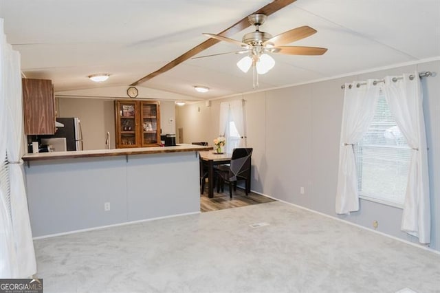 kitchen with vaulted ceiling with beams, kitchen peninsula, stainless steel fridge, and light carpet