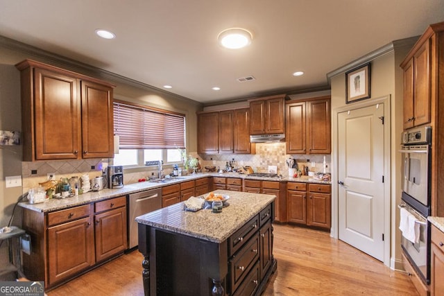 kitchen with appliances with stainless steel finishes, light wood-type flooring, ornamental molding, sink, and a kitchen island