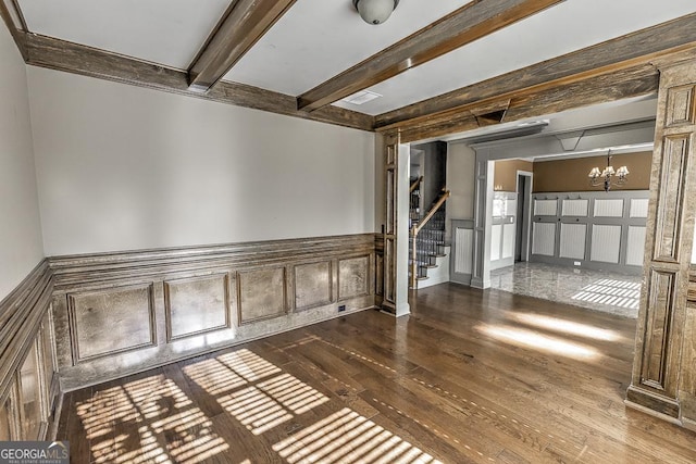 empty room with a chandelier, dark wood-style flooring, beamed ceiling, and stairs