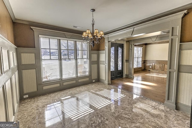 unfurnished dining area with a wainscoted wall, a chandelier, a decorative wall, and crown molding