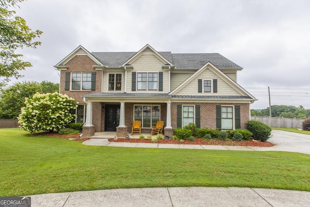 craftsman-style home featuring a shingled roof, fence, a front yard, a porch, and brick siding