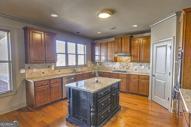 kitchen featuring under cabinet range hood, wood finished floors, a sink, visible vents, and appliances with stainless steel finishes