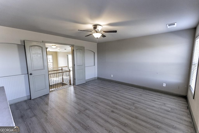 unfurnished room featuring a wainscoted wall, visible vents, ceiling fan, wood finished floors, and baseboards