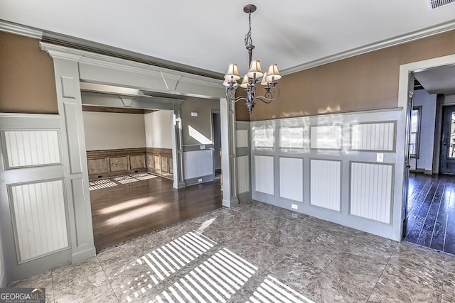 unfurnished dining area with a decorative wall, a wainscoted wall, visible vents, ornamental molding, and an inviting chandelier