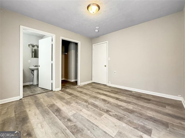 unfurnished bedroom featuring hardwood / wood-style flooring, connected bathroom, a textured ceiling, a walk in closet, and a closet