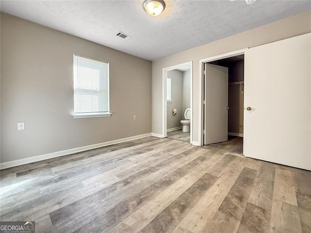 unfurnished bedroom with connected bathroom, light hardwood / wood-style flooring, a walk in closet, a textured ceiling, and a closet