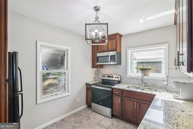 kitchen with hanging light fixtures, sink, light stone countertops, an inviting chandelier, and appliances with stainless steel finishes