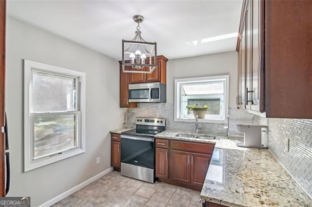 kitchen with hanging light fixtures, sink, appliances with stainless steel finishes, light stone counters, and tasteful backsplash