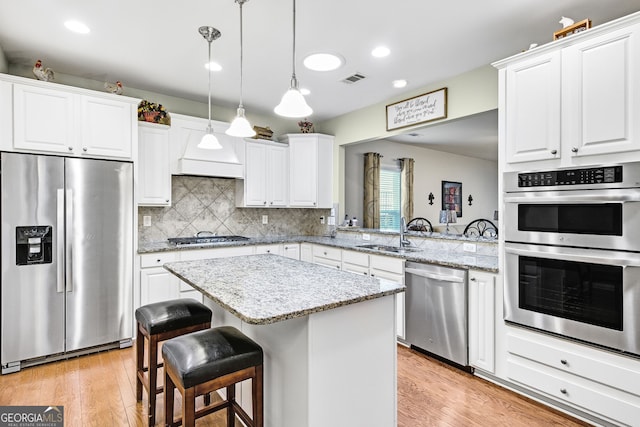 kitchen with light wood finished floors, decorative backsplash, appliances with stainless steel finishes, a sink, and a kitchen island