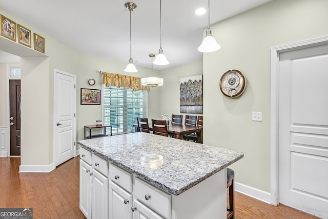 kitchen featuring a kitchen island, wood finished floors, baseboards, white cabinetry, and pendant lighting